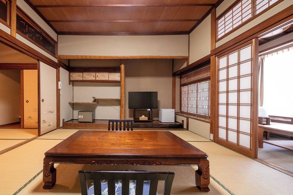 Une pièce de style japonais traditionnel, avec un sol recouvert de tatamis, une table en bois, un téléviseur et des portes coulissantes.