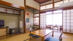 A traditional Japanese room with tatami flooring, a low table, chairs, a television, and sliding doors. - Takezono Ryokan (Shimonoseki)