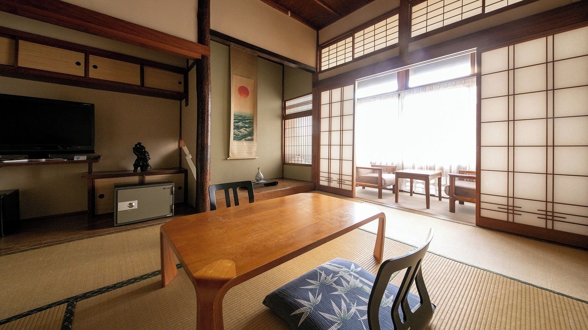 A traditional Japanese room with tatami flooring, a low table with cushions, a TV, and sliding doors.