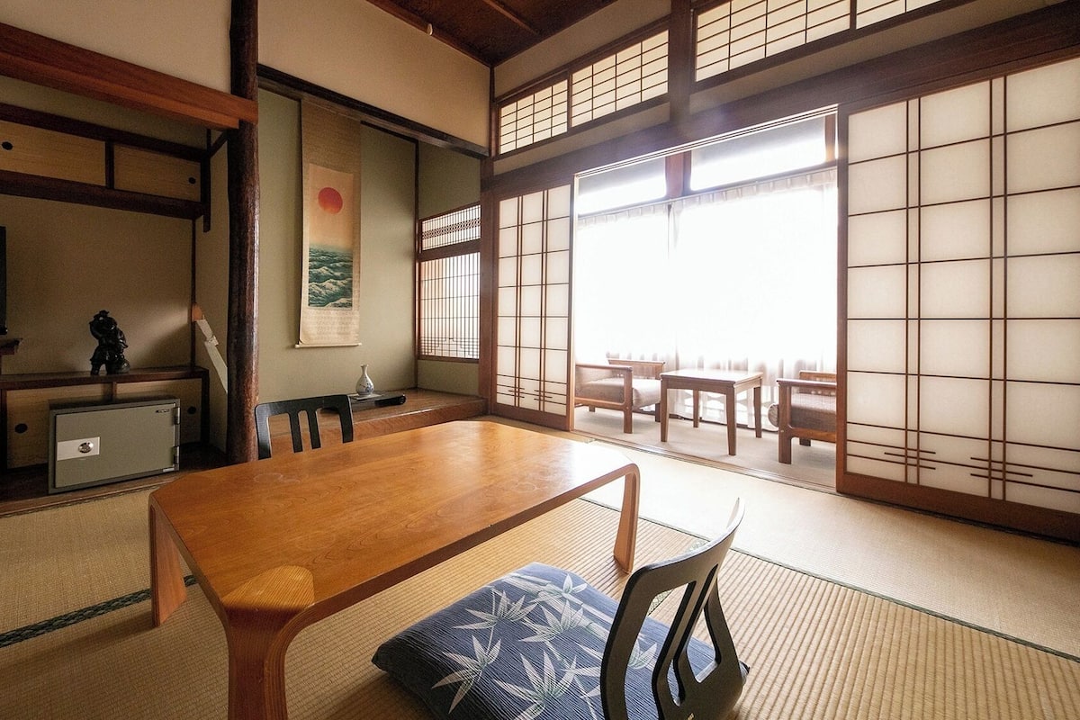 Une pièce de style japonais traditionnel, avec un sol recouvert de tatamis, une petite table basse avec des coussins, un téléviseur et des portes coulissantes.