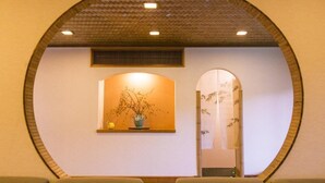 A reception area with a circular archway, a wooden ceiling, a wall-mounted plant, and a mirror. - Takezono Ryokan (Shimonoseki)