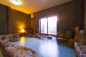 A traditional Japanese onsen with a wooden interior, a stone bath surrounded by rocks, and a sliding door leading to the outside. - Takezono Ryokan (Shimonoseki)