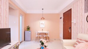 A modern living room with a flat-screen TV, a coffee table with a vase of flowers, a dining area with a white table and chairs, and a sofa with a fluffy pillow. - Shenzhen Maiya Apartment (Shenzhen)
