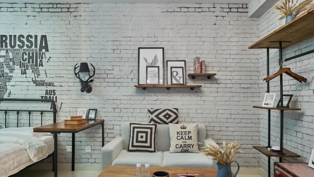 A modern living room with a white brick wall, a sofa with decorative pillows, a coffee table with books and a vase, and a hanging lamp. - Shenzhen Maiya Apartment (Shenzhen)