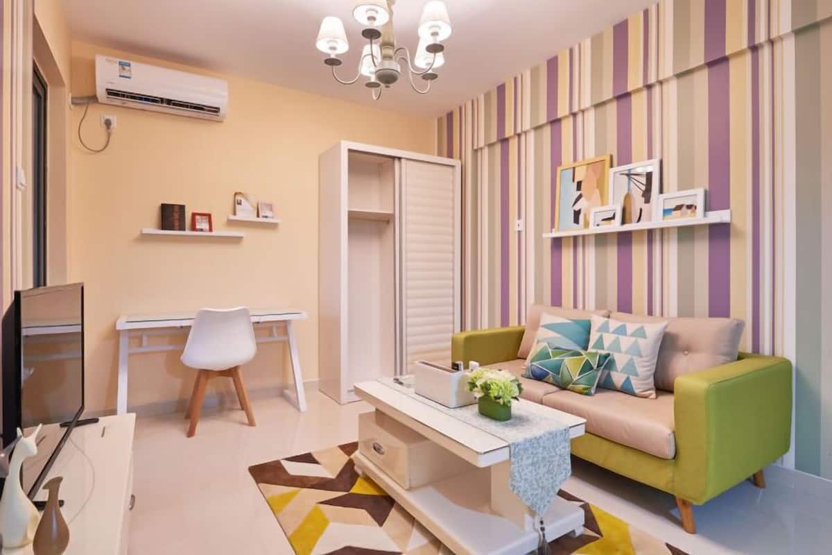A modern living room with a sofa, a coffee table, a TV, a desk, and a wardrobe.
