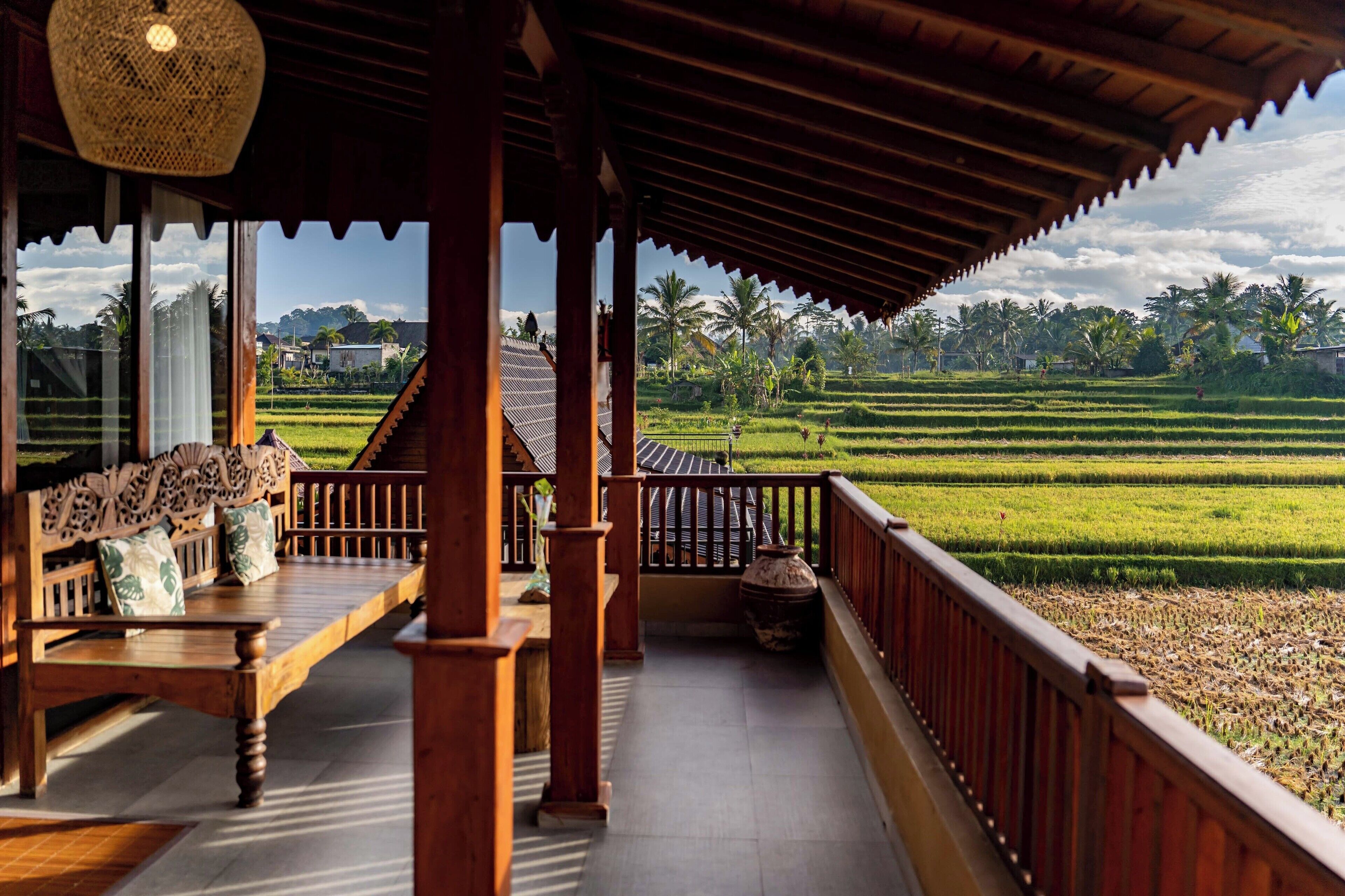 A traditional wooden balcony with a view of terraced rice fields and palm trees.