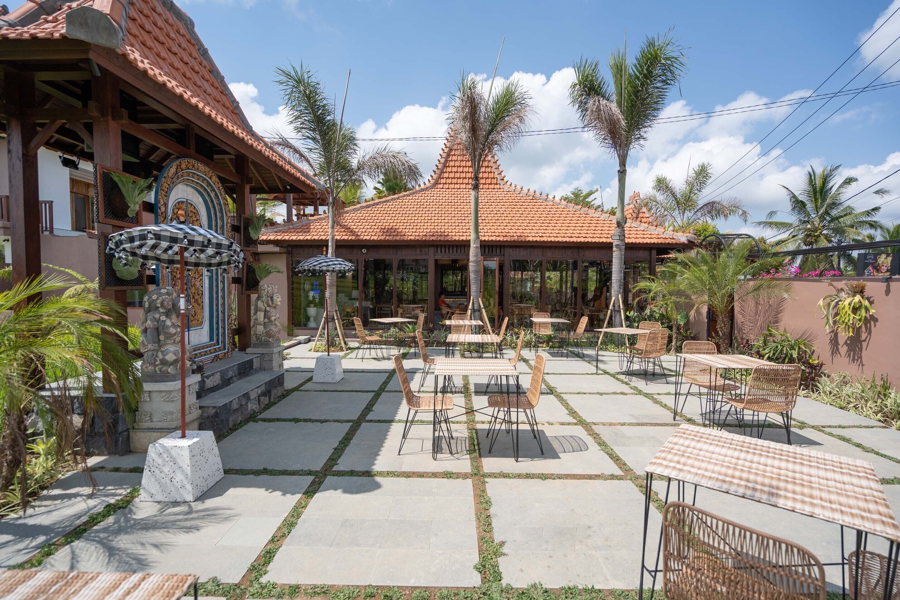 Un patio al aire libre con mesas y sillas, un espacio de estar techado y un edificio con techo de tejas.