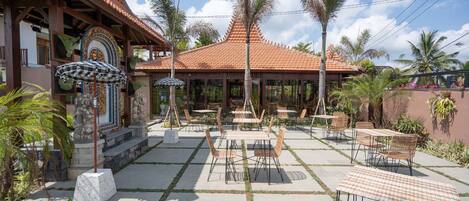 Un patio al aire libre con mesas y sillas, un espacio de estar techado y un edificio con techo de tejas.