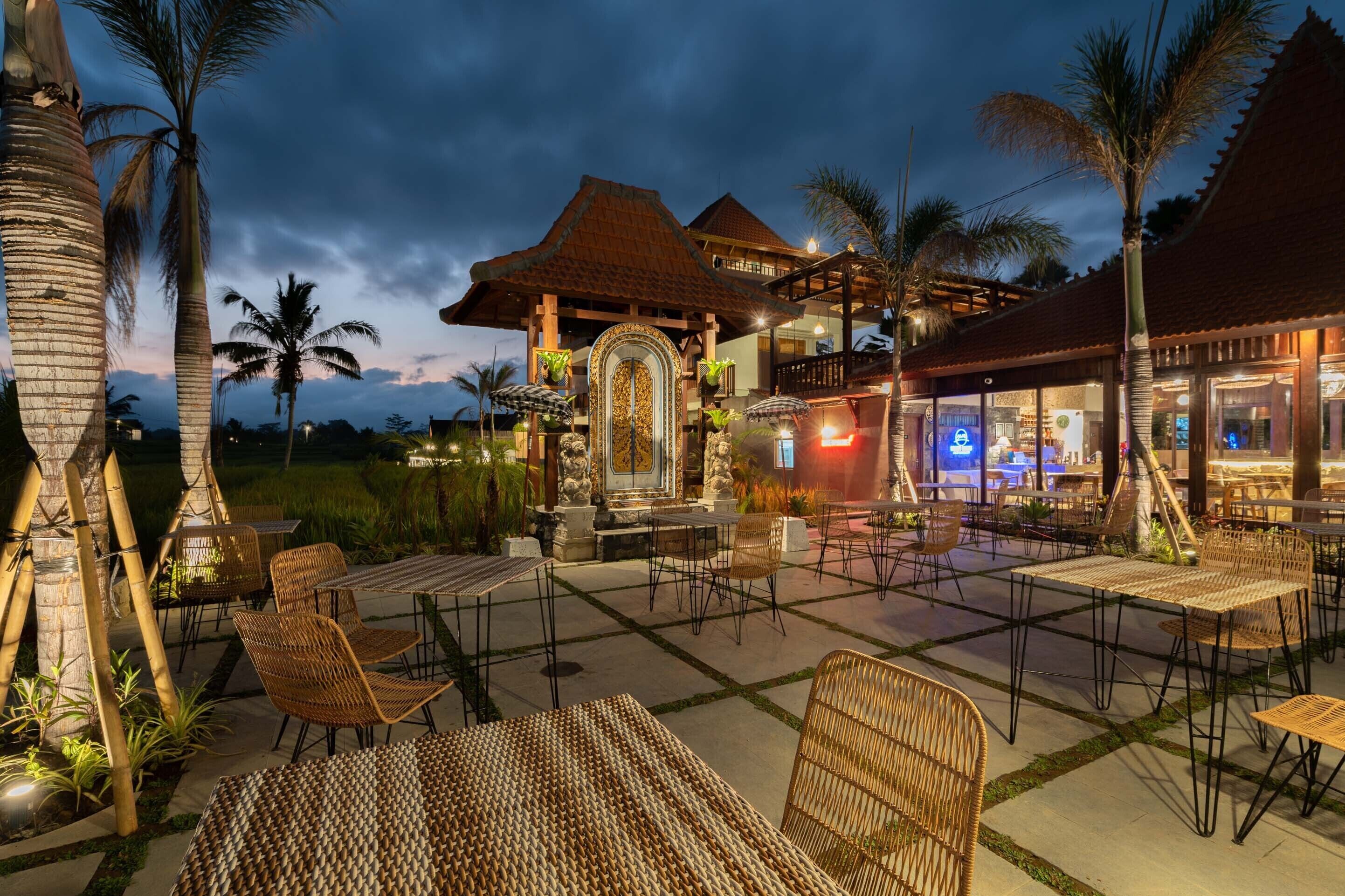 Ein möblierter Patio-Bereich im Freien mit Korbmöbeln, einem steinernen Bogen und einem Restaurant mit Neonreklame.