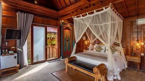 A wooden cabin-style bedroom with a four-poster bed, a television, and a small refrigerator.
