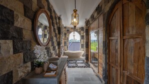 A stone-walled hallway with a large mirror, a stone bathtub, and a wooden door.