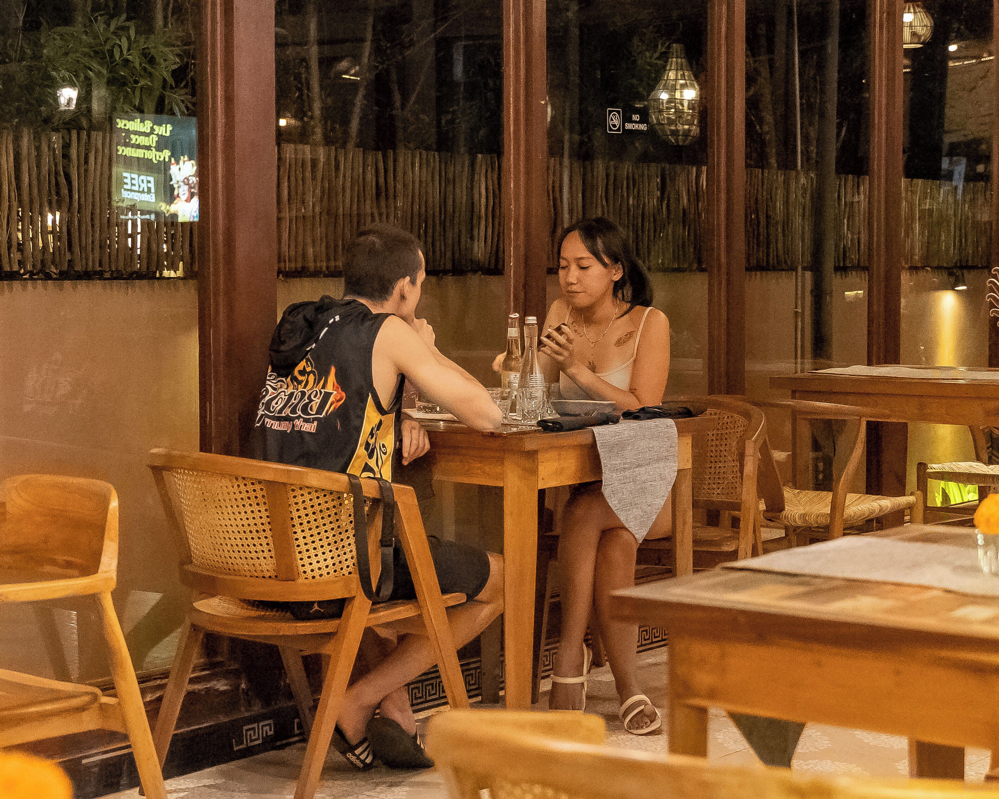 A restaurant with wooden furniture, a table with a bottle and glasses, and a person sitting at the table.