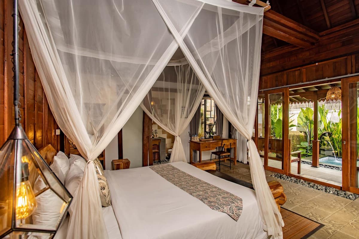 A bedroom with a canopy bed, wooden furniture, and a view of a garden.