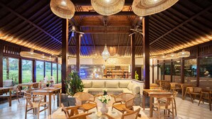 A spacious lobby with wooden furniture, a central seating area, and large windows offering a view of the outdoors.