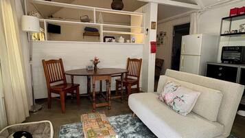 A compact living space with a dining area, sofa, pet bed, and a patterned rug.
