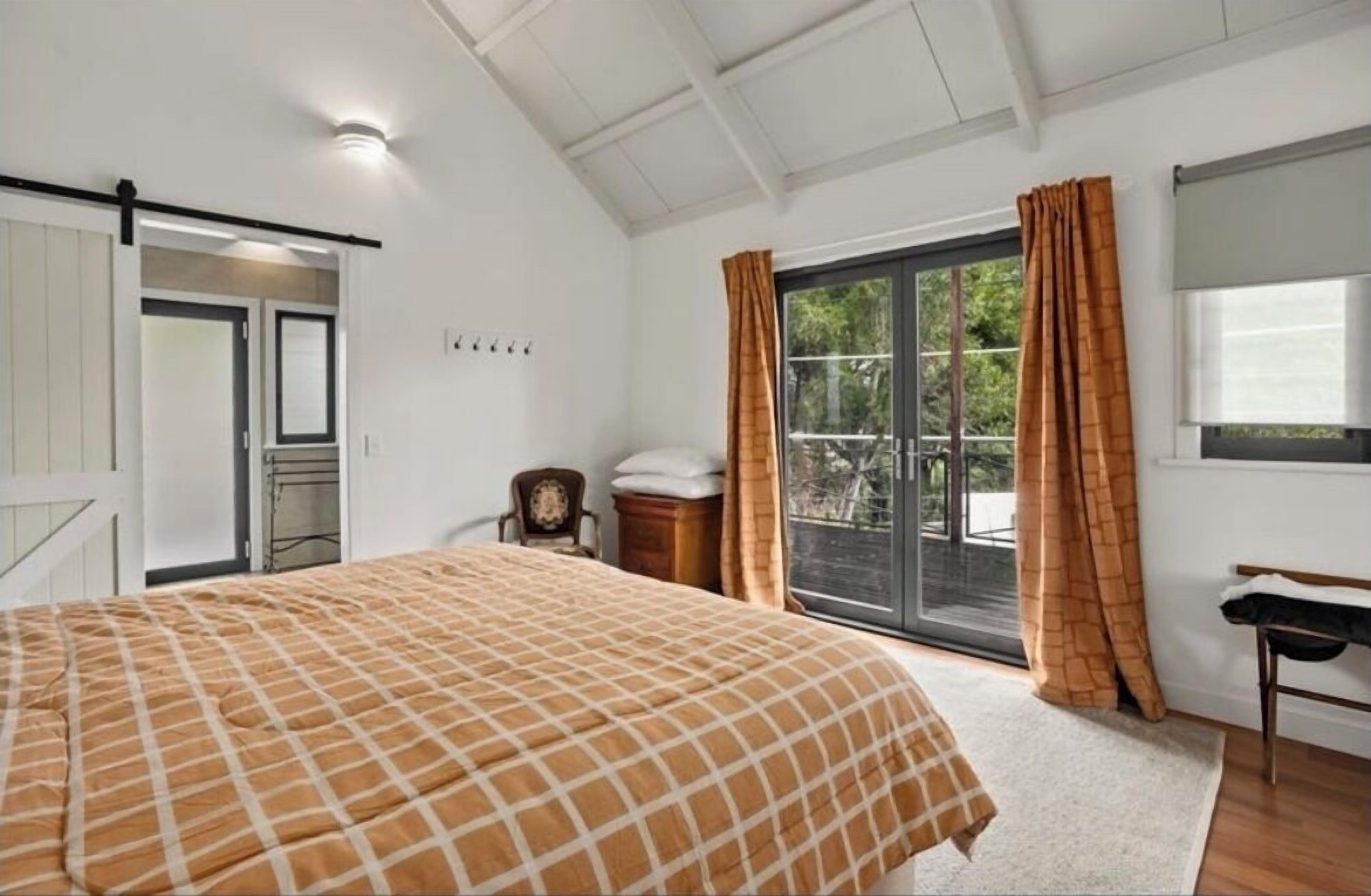 A bedroom with a bed, a window with curtains, a door, and a small table.