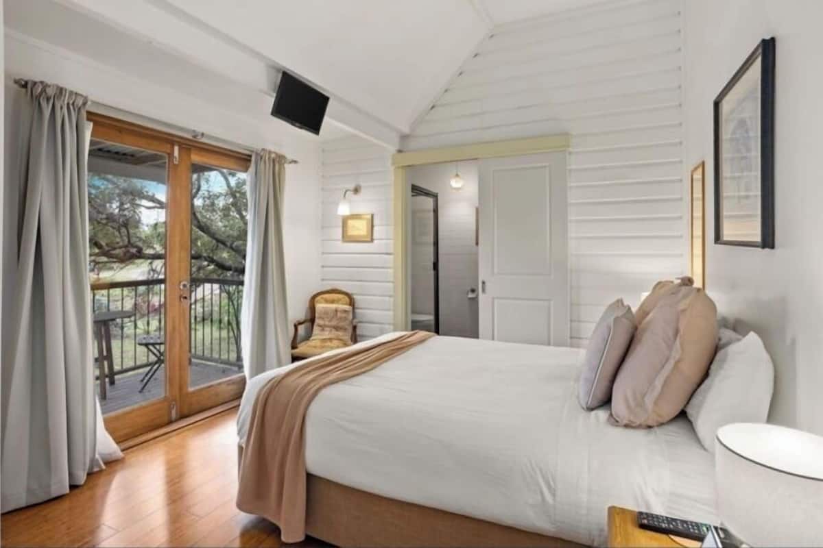 A bedroom with a bed, a chair, a TV, and a balcony.