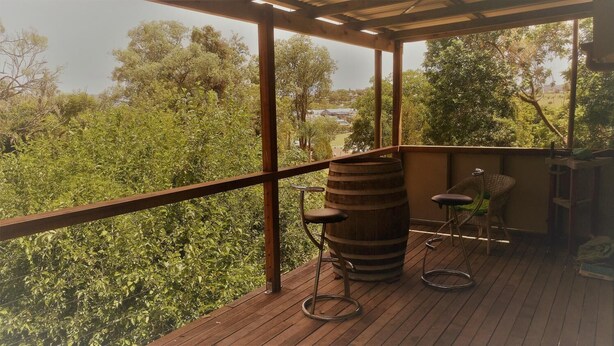 A wooden deck with a rustic barrel, two bar stools, and a wicker chair. - Boonah Cottage (Boonah)