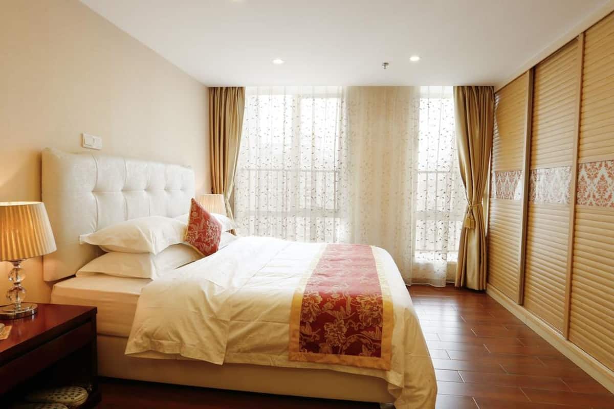 A hotel room with a large bed, a bedside table with a lamp, and a window with curtains.