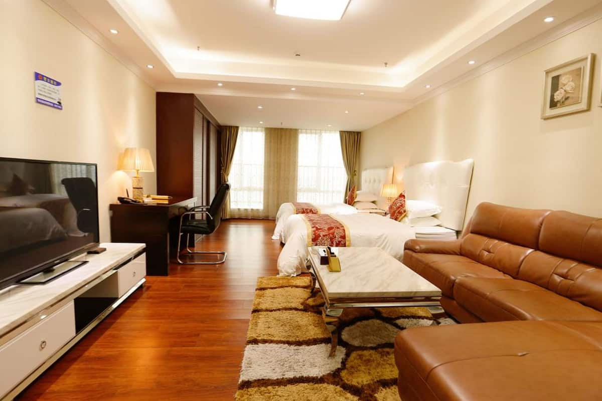 A hotel room with a TV, two beds, a sofa, a desk, and a large window with curtains.