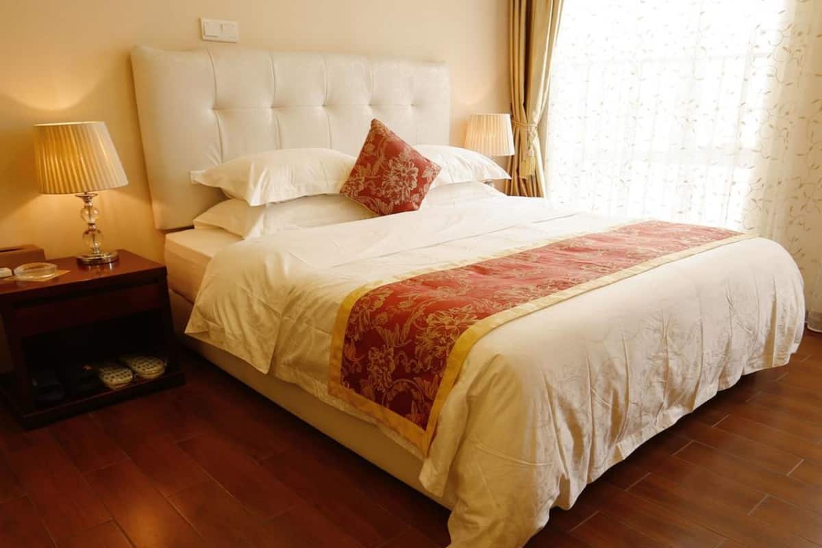 A neatly made bed with a white headboard, a red and gold throw blanket, and a wooden nightstand with a lamp.