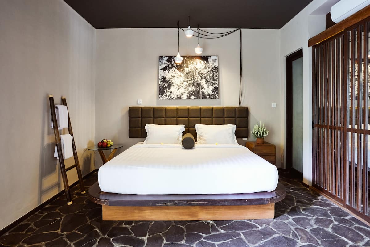 A bedroom with a large bed, a headboard, a nightstand, a wall-mounted picture, and a wooden floor.