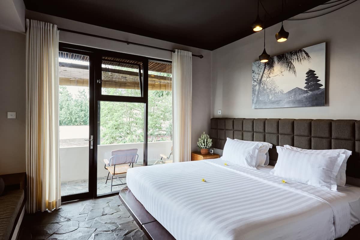 A bedroom with a large bed, a view to a balcony, and a painting on the wall.