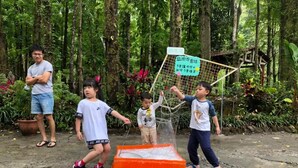 Un grupo de niños jugando con una red y un contenedor naranja grande en un área boscosa.
