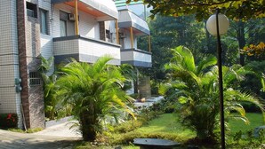 Un edificio residencial con fachada de tejas, un balcón y un jardín con palmeras y un sendero.