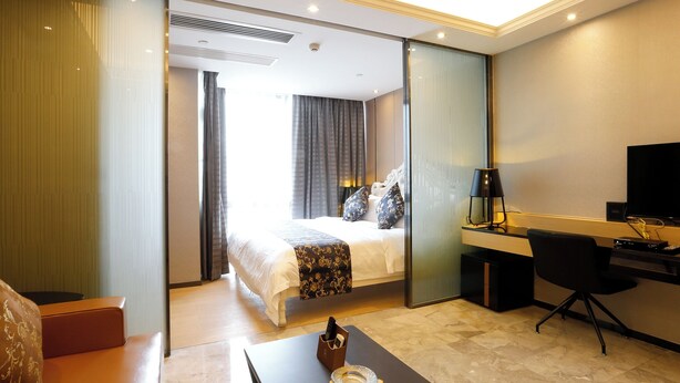 A hotel room with a bed, a desk with a computer, a TV, and a seating area with a table and chairs. - Pengman International Apartment Hotel (Guangzhou)