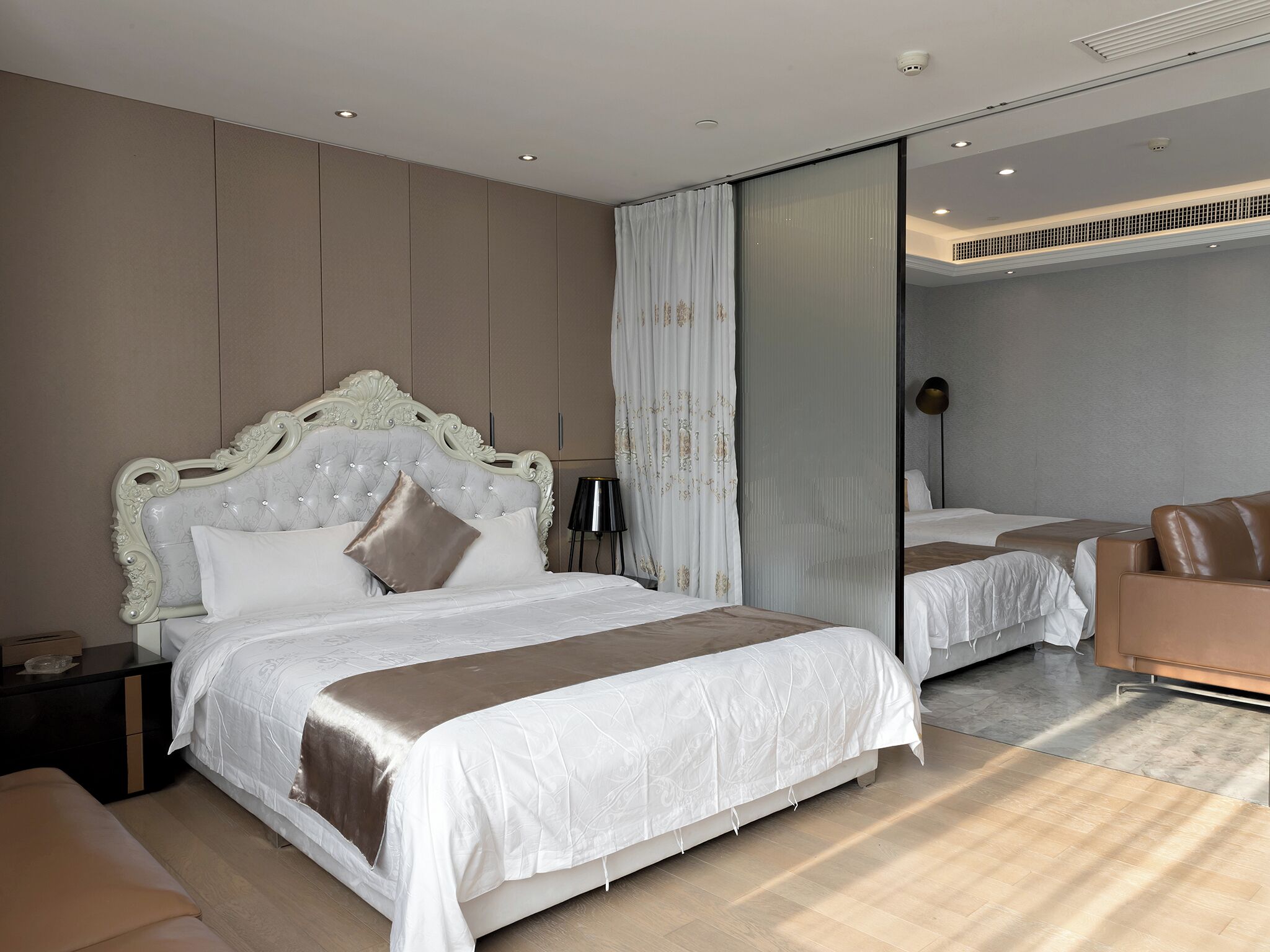A modern bedroom with a large bed, a smaller bed, a sofa, and a mirror.