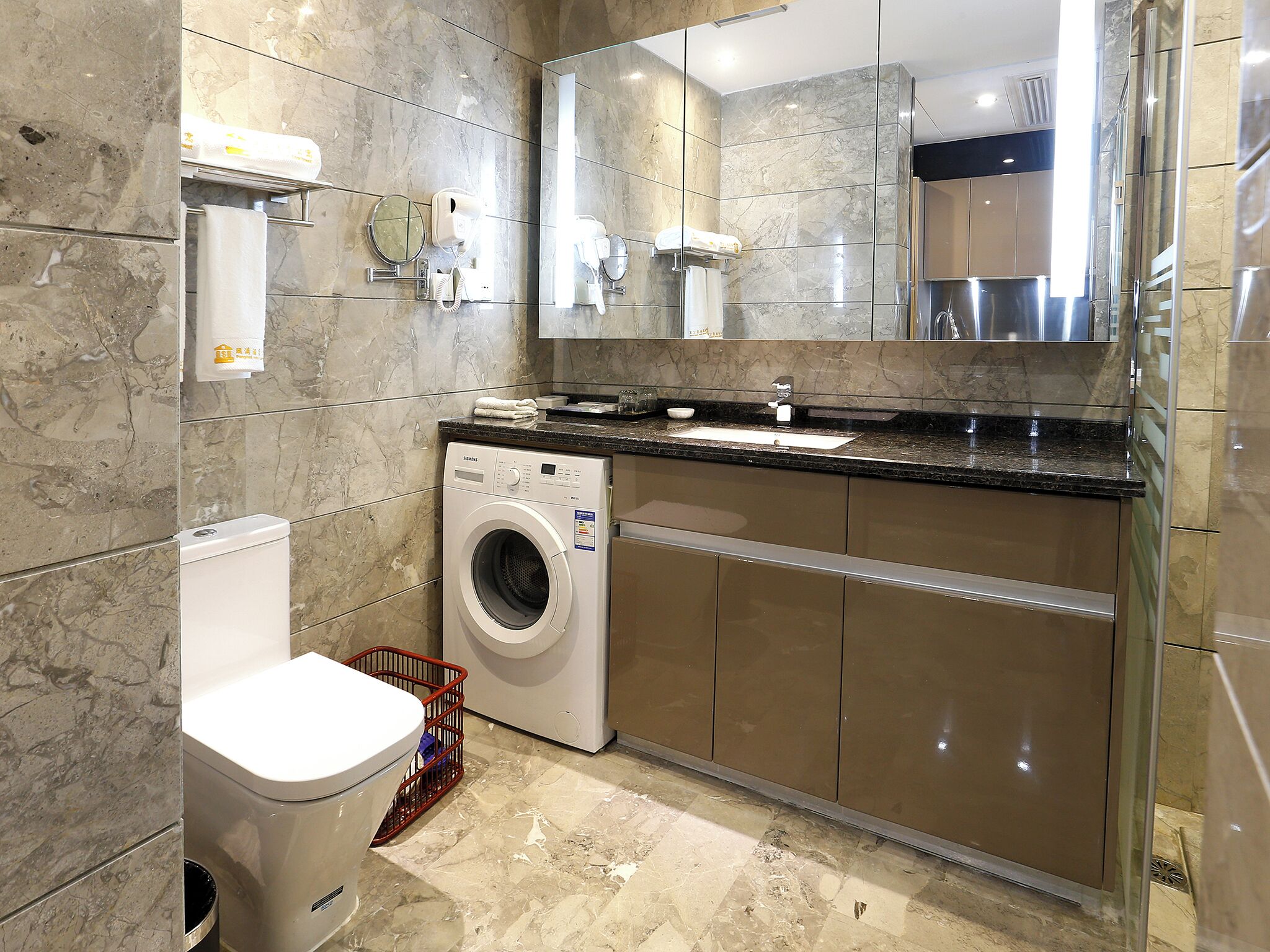 A modern bathroom with a washing machine, toilet, and a large mirror.