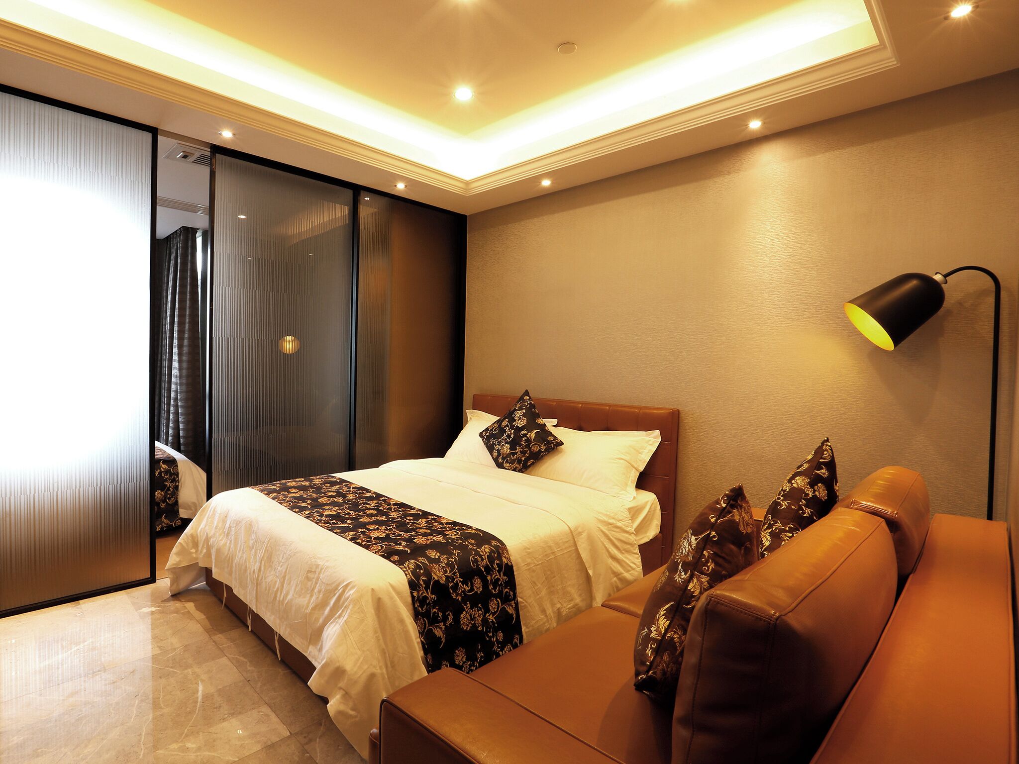 A modern hotel room with a large bed, a sofa, a desk, and a sliding door leading to a balcony.