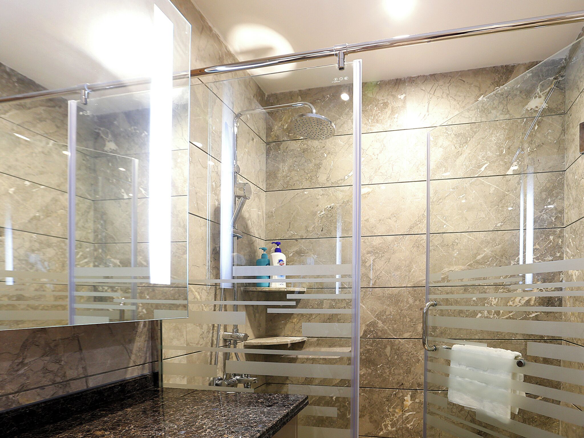 A modern bathroom with a glass-enclosed shower, marble walls, and a granite countertop.