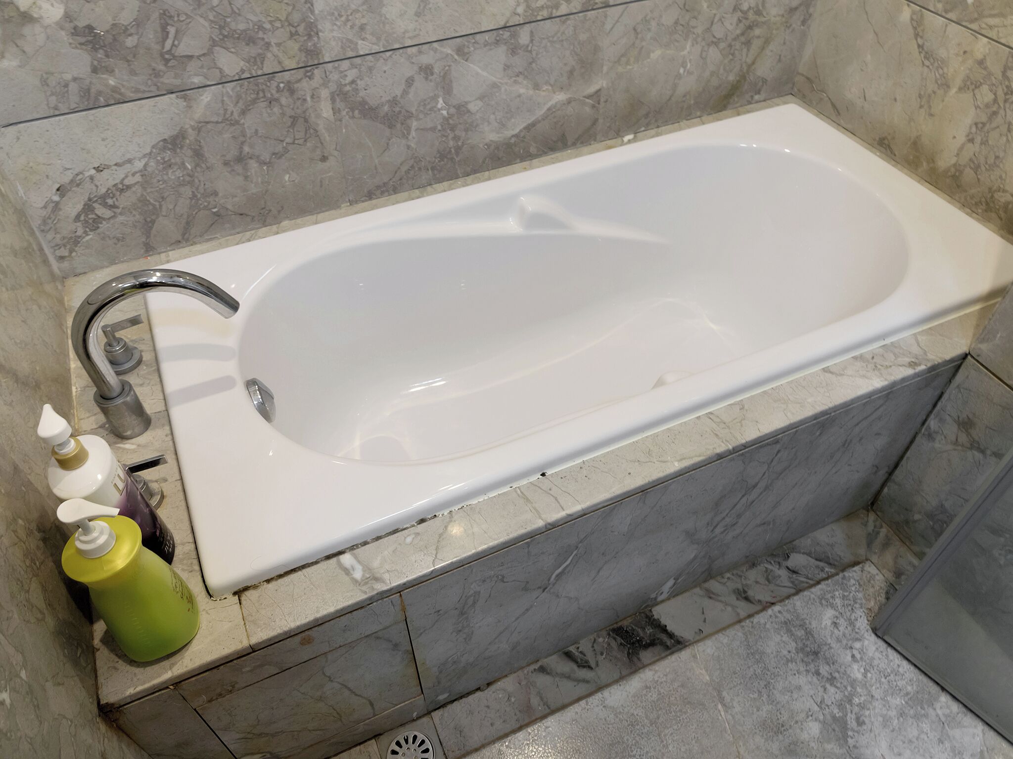 A bathroom with a white bathtub, a chrome faucet, and a marble wall.