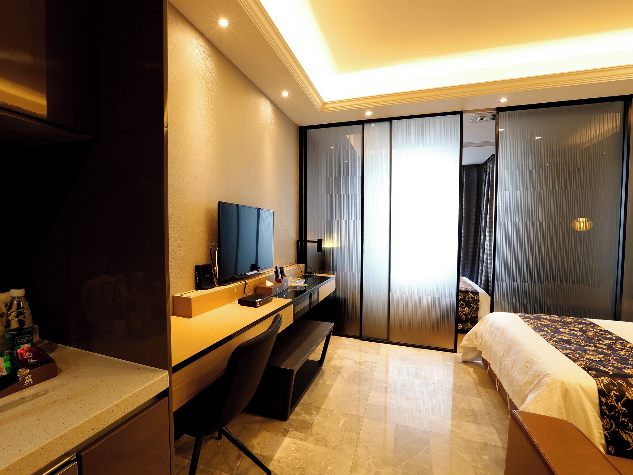 A hotel room with a bed, a desk with a computer, a TV, and a minibar.