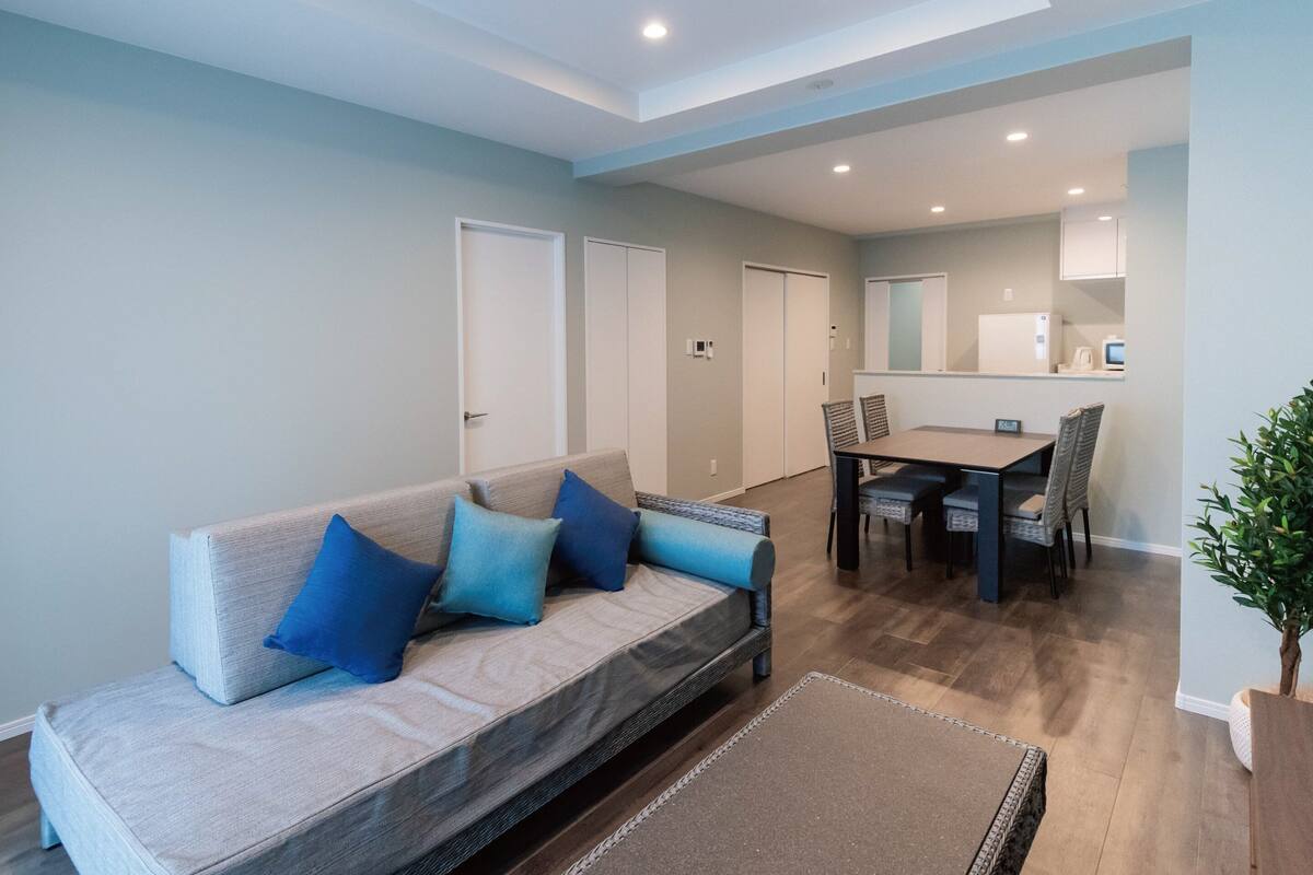 A modern living room with a sofa, dining table, chairs, and a small kitchen area.