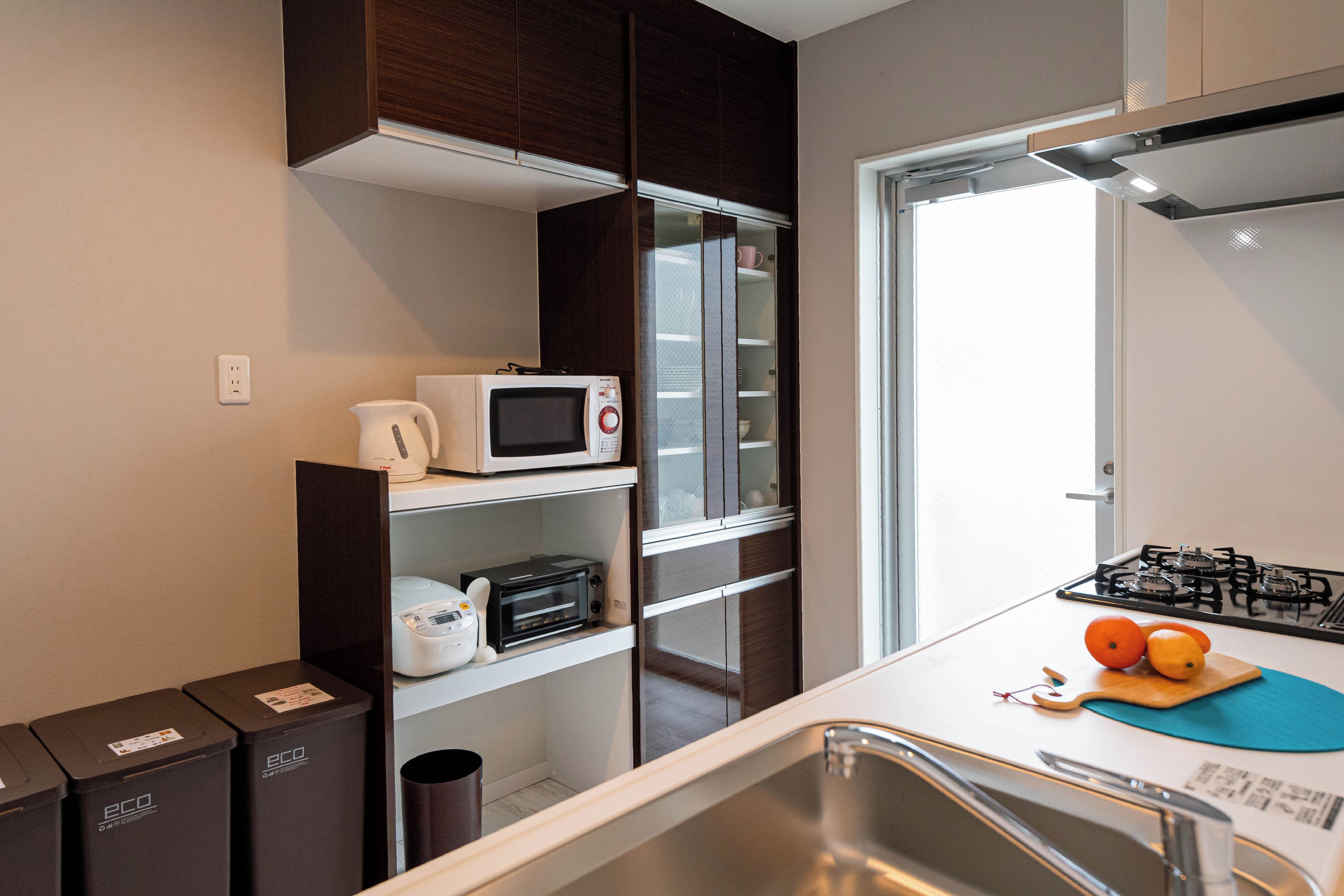 A compact kitchen with a microwave, kettle, and toaster on shelves, a gas stove, and a sink.