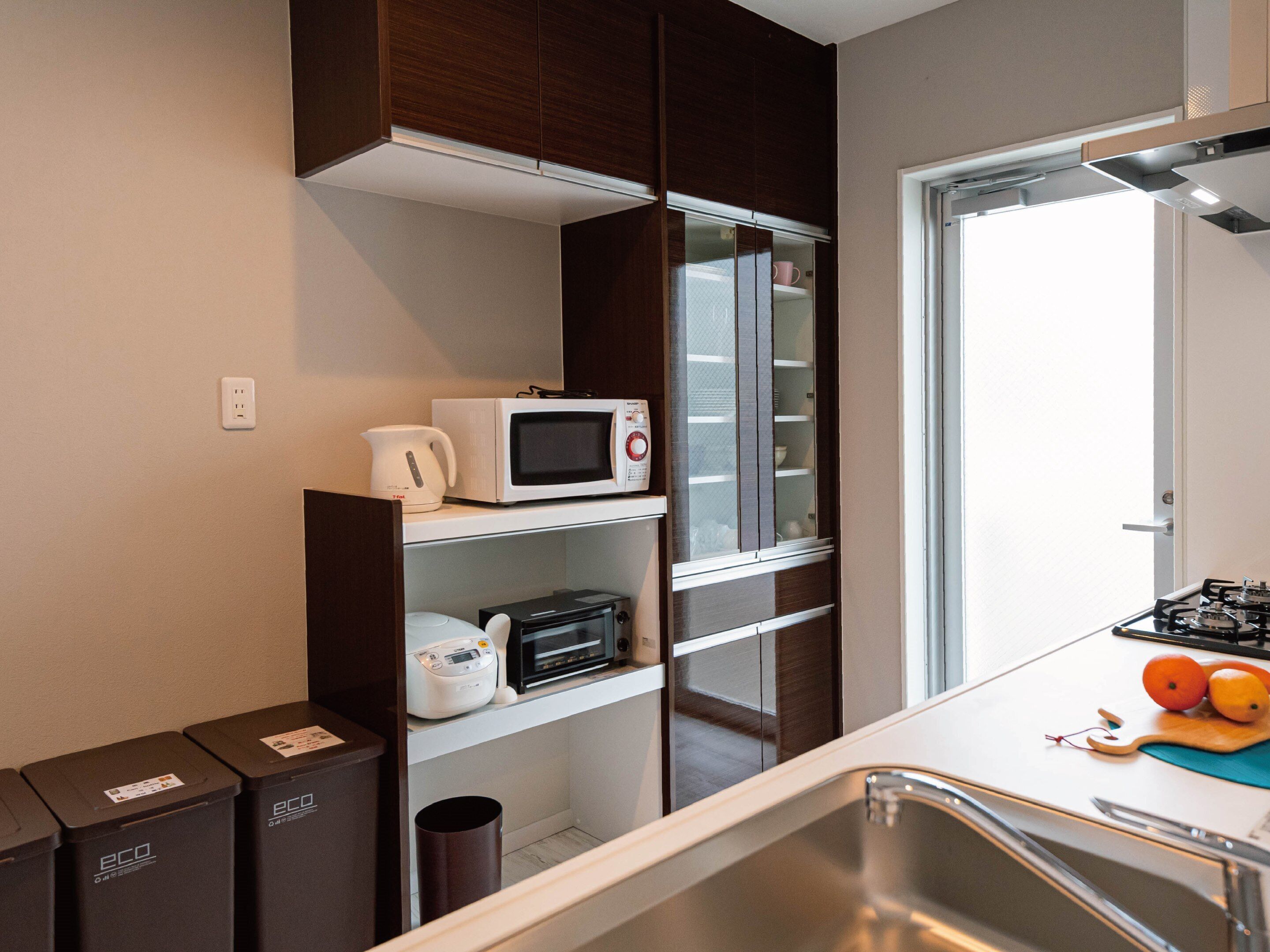 A compact kitchen with a microwave, kettle, and toaster on the counter, a sink, and a window with a view.