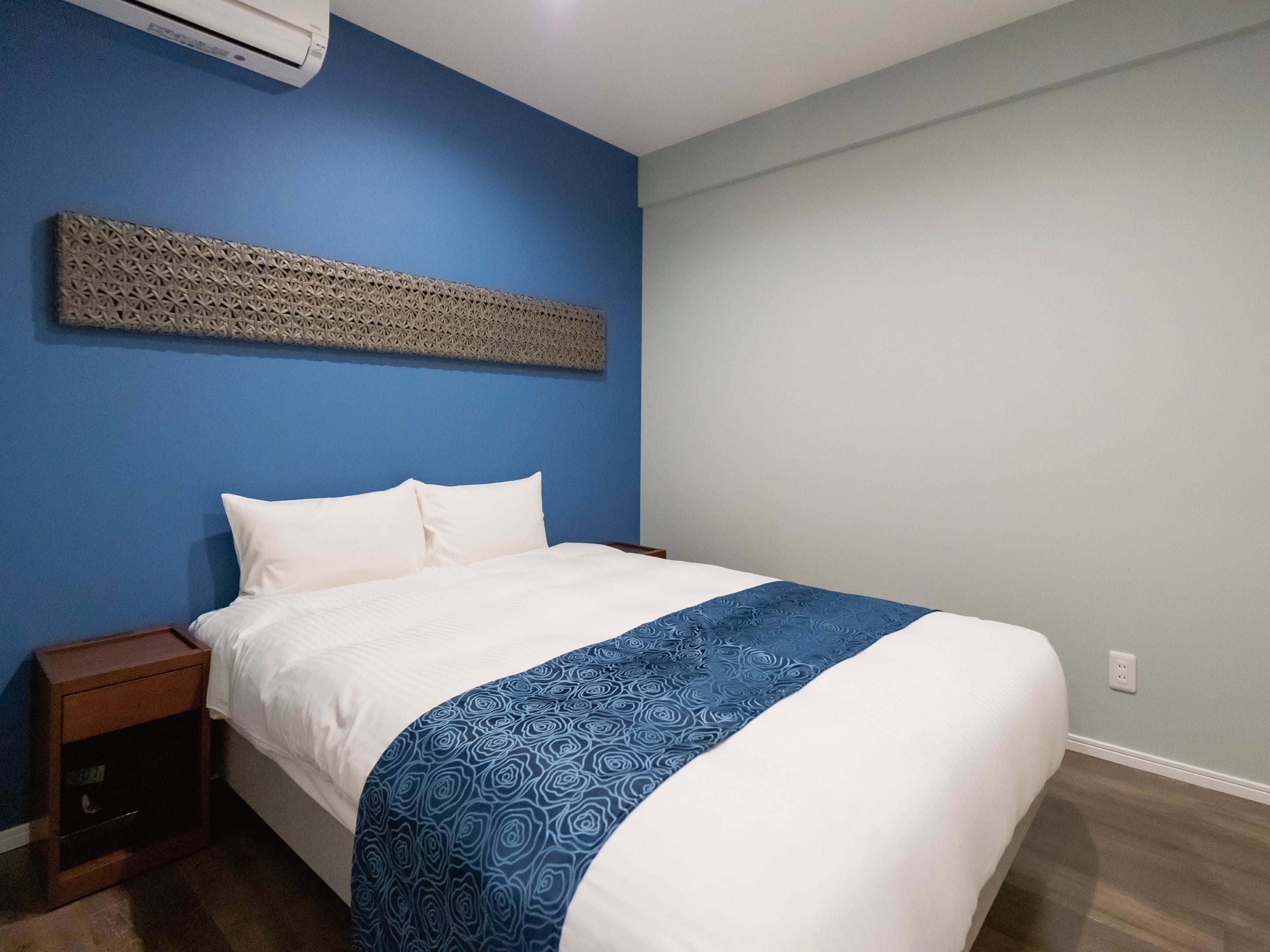 Une chambre à coucher comprenant un lit, une table de chevet, un climatiseur fixé au mur et un élément décoratif mural.
