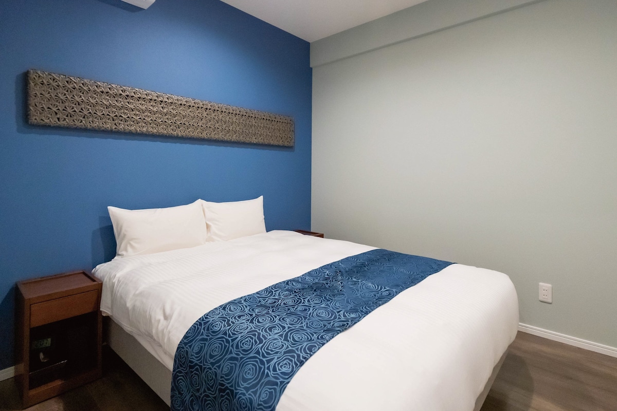 A bedroom with a bed, a nightstand, a wall-mounted air conditioner, and a decorative wall piece.
