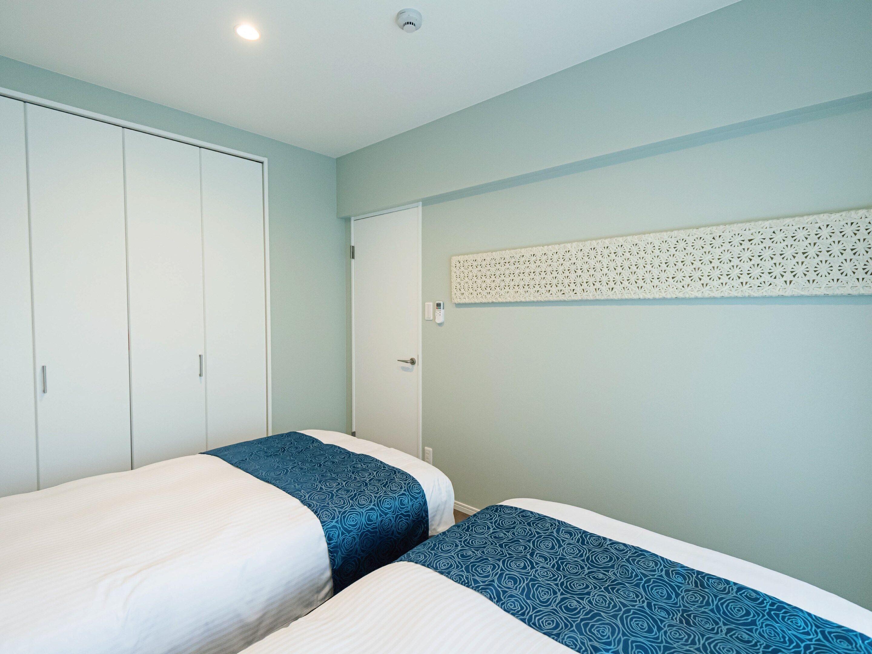 Une chambre avec deux lits, une armoire et un panneau décoratif au mur.