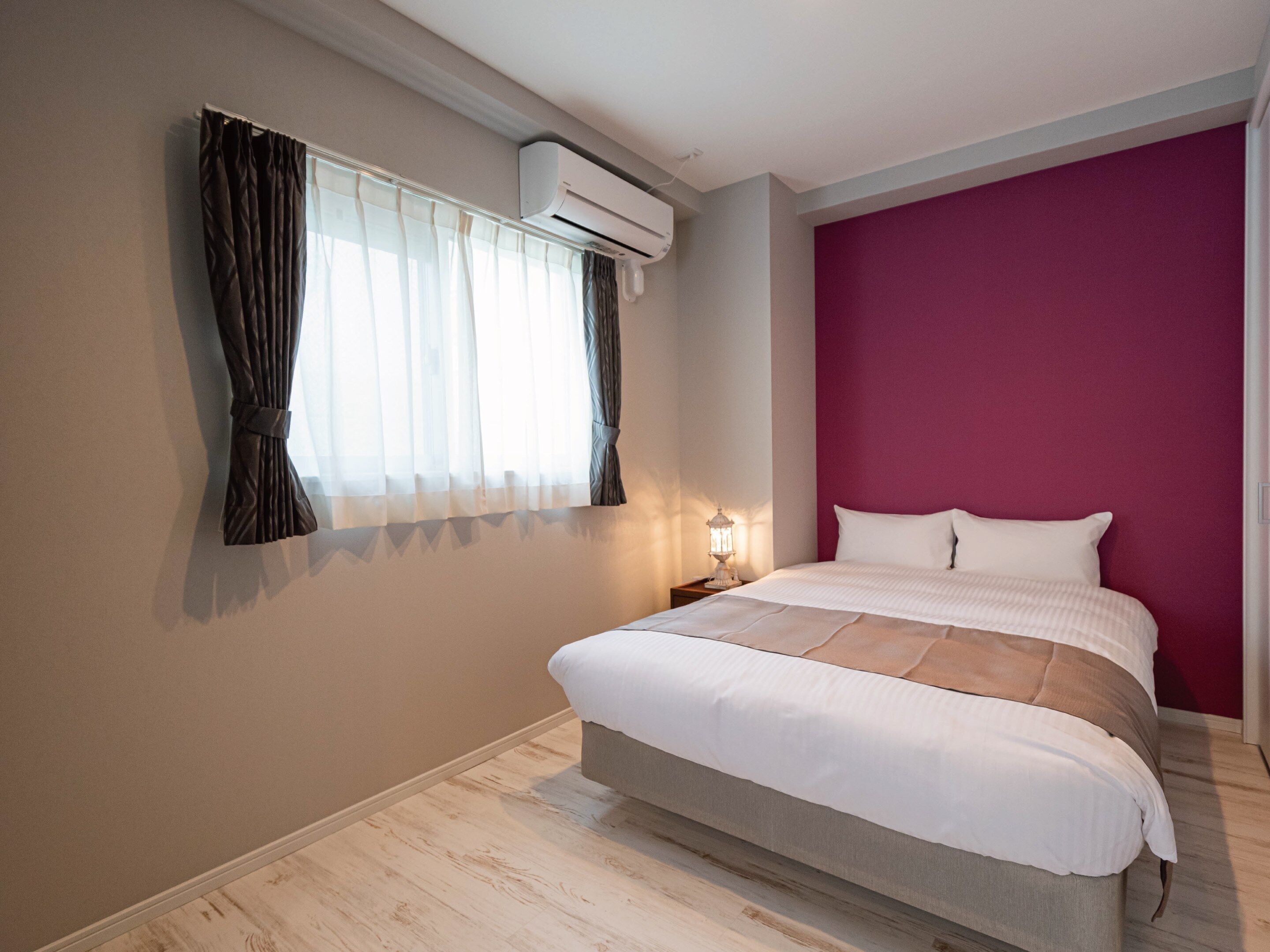 Un dormitorio con cama, mesita de noche, aire acondicionado y ventana con cortinas.