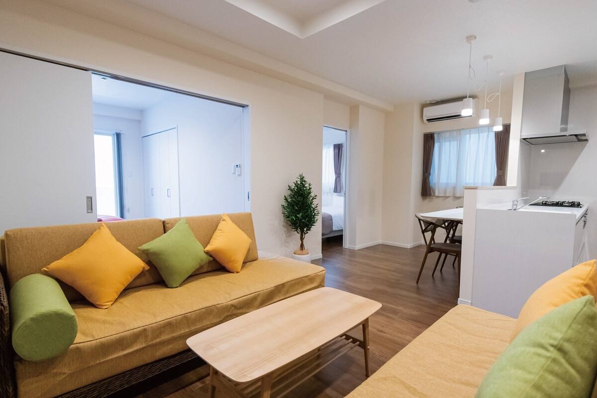 A modern living room with a sofa, a small table, and a view into a bedroom.