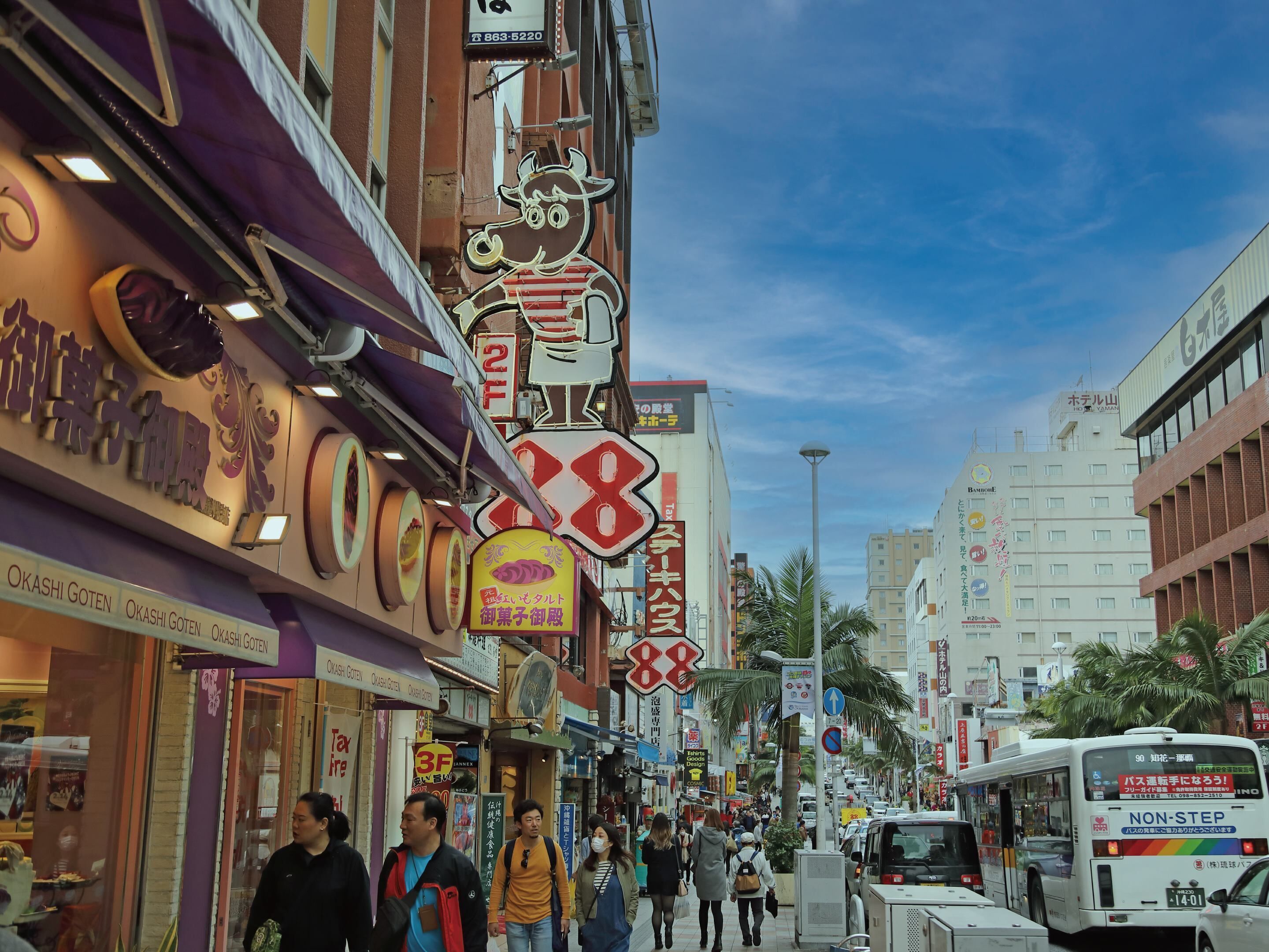 A busy urban street with various shops and signs, including a prominent '88' sign and a 'NON-STEP' bus.