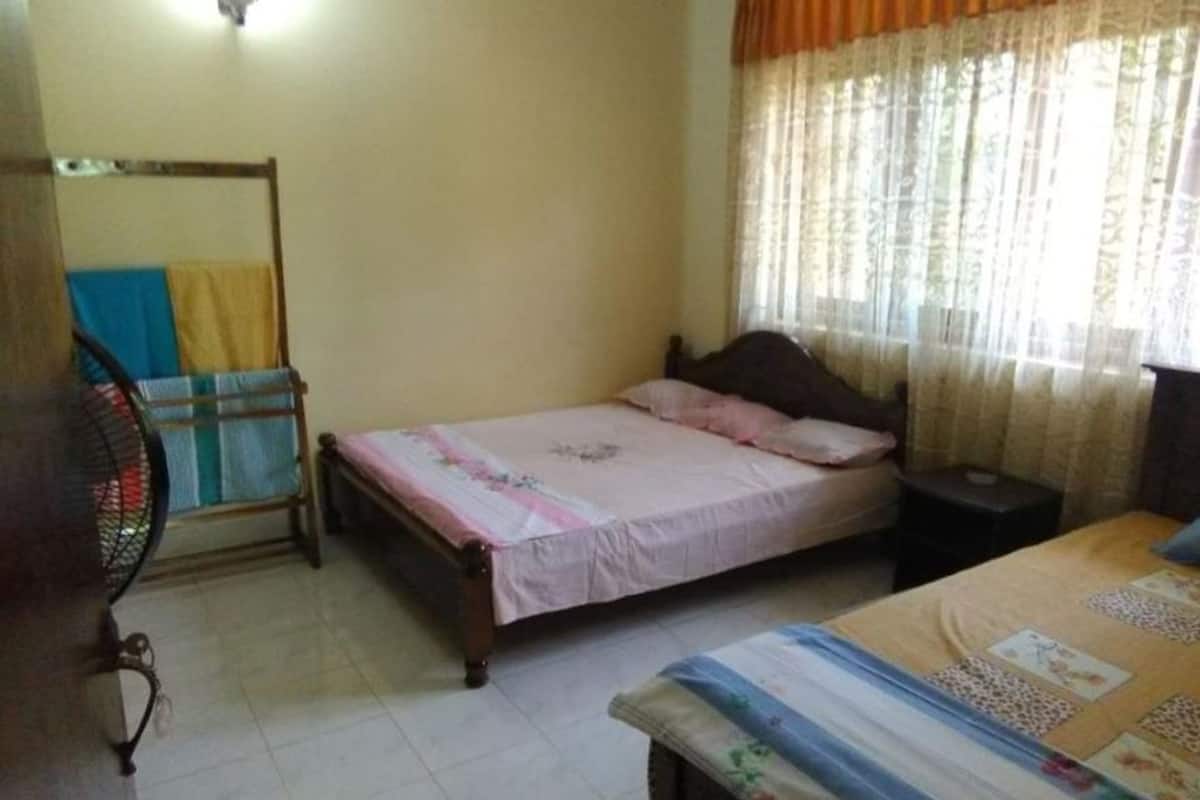 Un dormitorio con una cama individual, una mesita de noche, un armario de madera y un ventilador de pie.