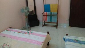 Un dormitori amb un llit, un ventilador de peu, un mirall i una prestatgeria de fusta amb tovalloles de colors.