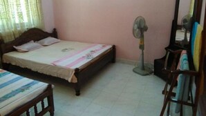 Un dormitori amb un llit, un ventilador de peu, un mirall i una cadira.
