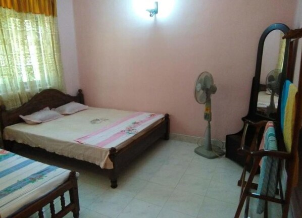A bedroom with a bed, a standing fan, a mirror, and a chair.