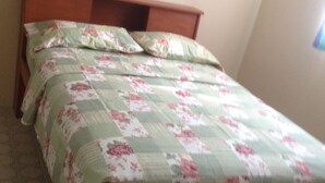 A bed with a floral bedspread and wooden headboard in a room with patterned flooring. - Liamuiga Drive Inn (Basseterre)